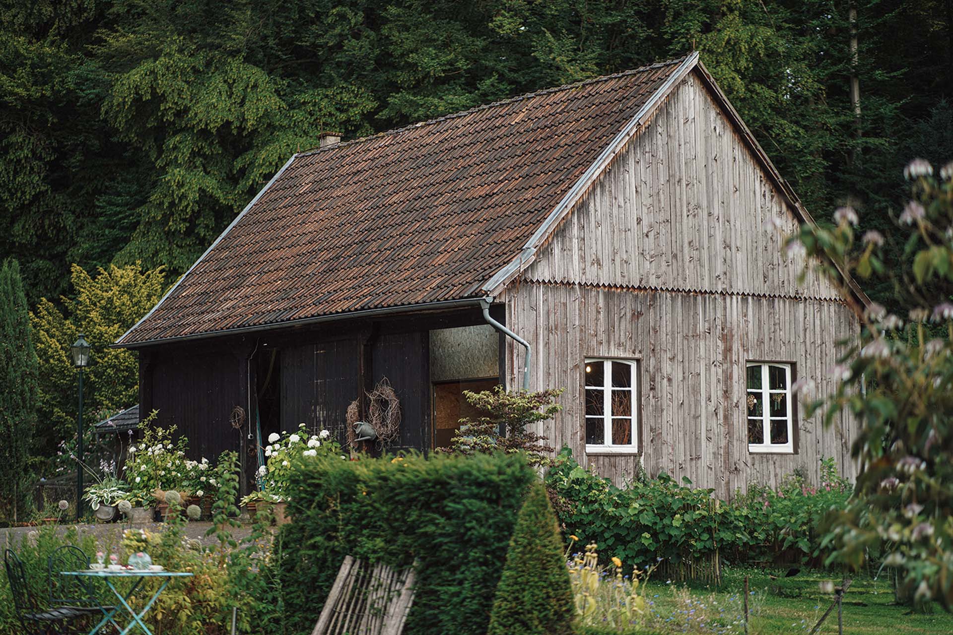 Historisches holzverkleidetes Gebäude zwischen blühenden Beeten und grünen Gartenhecken im Mühlengarten